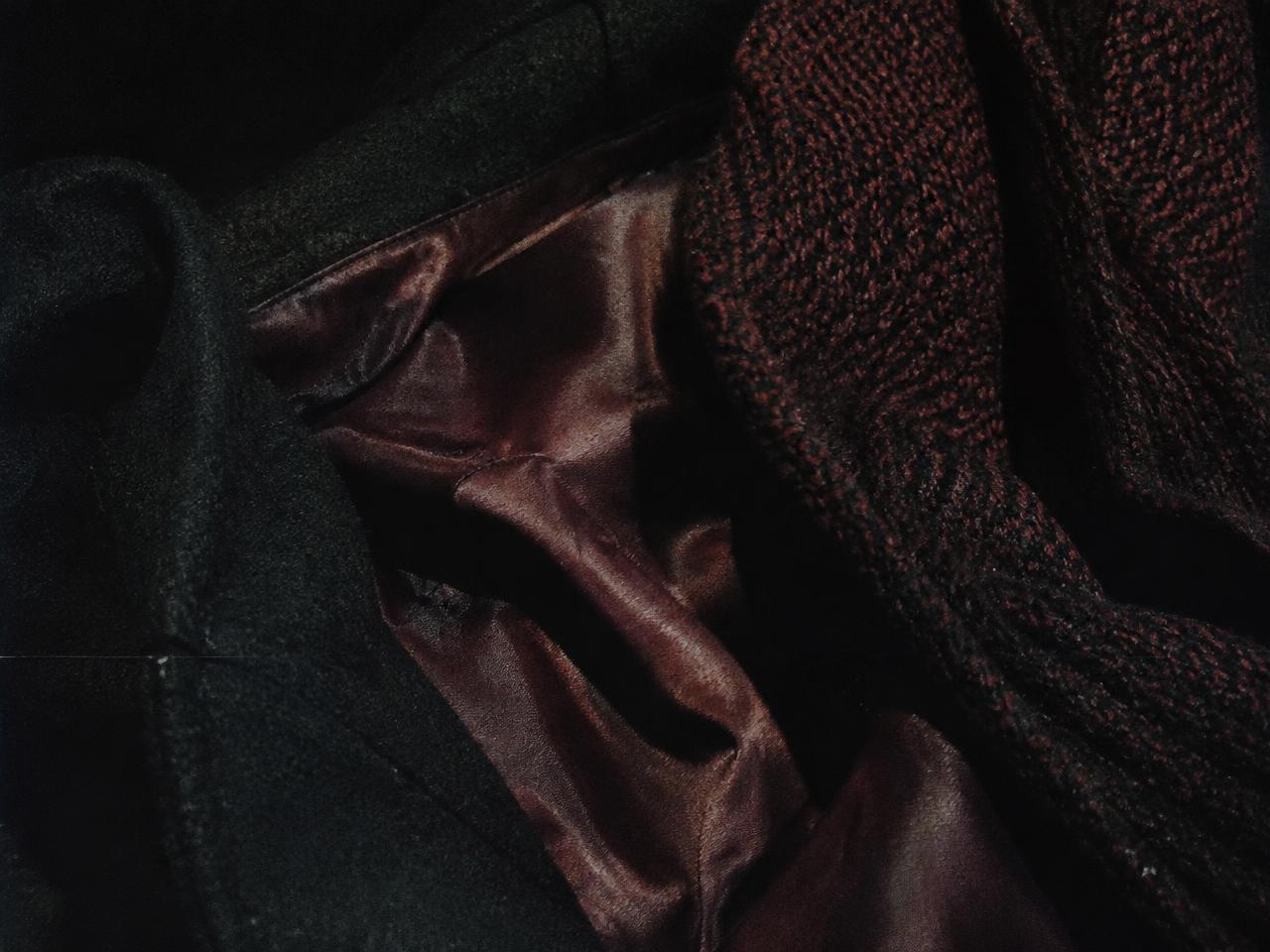 Close-up of a dark wool coat with an oxblood silk lining beside a knitted scarf