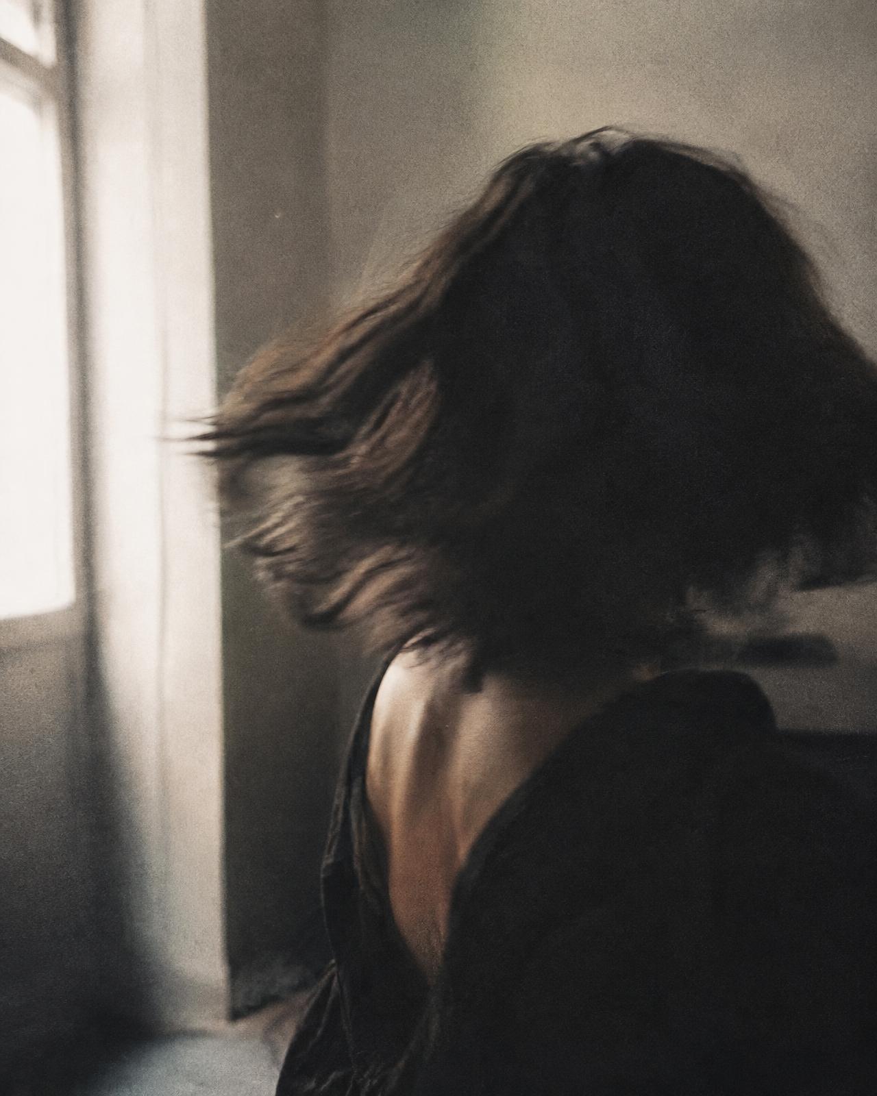 Dark hair blurred in motion as a woman turns away from a window