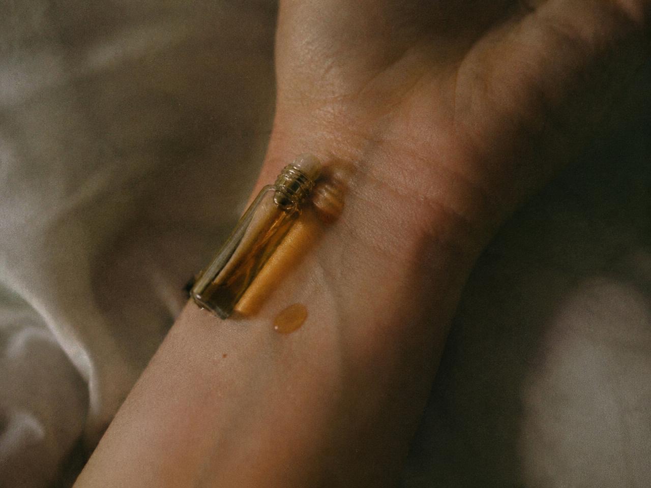 Small roll-on perfume oil vial resting on an inner wrist beside a drop of amber oil