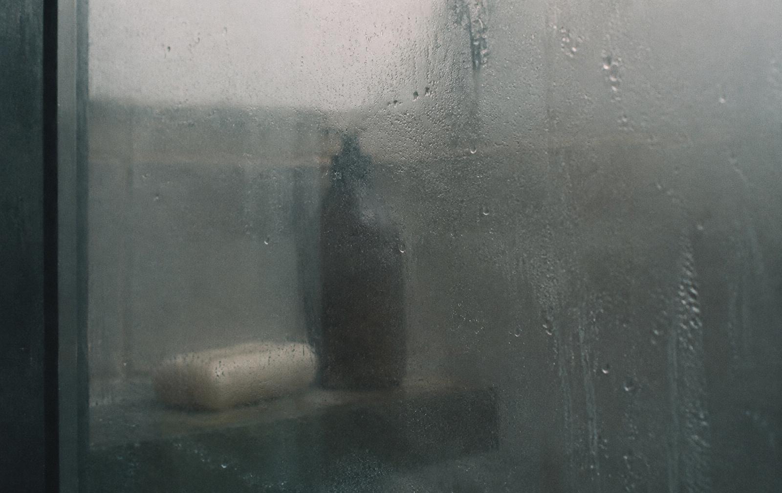 Fogged shower glass with droplets, a bar of soap and a body-wash bottle blurred behind it